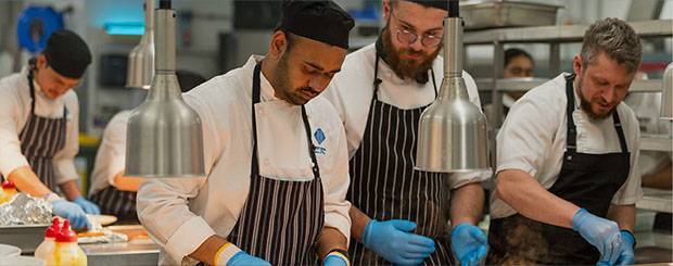 Professional chefs in uniform and gloves, preparing dishes in the Wrest Point Hotel kitchen.