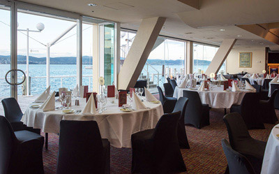 Interior of the Boardwalk Gallery at Wrest Point Hotel Casino, with white tablecloth round tables and a waterfront view.