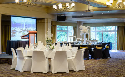 Interior of the Derwent Room at Wrest Point Hotel, with elegant round tables, chandeliers and a projector screen.